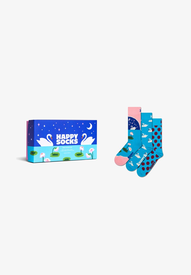 Pudełko prezentowe obok trzech kolorowych skarpetek z wzorami przedstawiającymi łabędzie, lilie wodne, kropki i nocne niebo na białym tle.