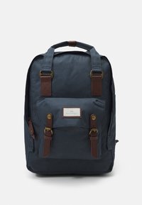 Marineblauwe rugzak met bruine leren accenten, voorzien van twee voorzakken, verstelbare schouderbanden en een handvat aan de bovenkant. Gladde stoftextuur.