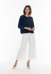 Navy-blaues Langarmoberteil mit lockerer Passform, kombiniert mit weißen, weit geschnittenen Hosen und hellen Schuhen. Minimalistisches Design, glatte Textur.