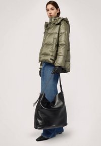 Svart hobo-väska i läder med en mjuk textur och avslappnad design, utrustad med en enkel axelrem och diskret märkning framtill.