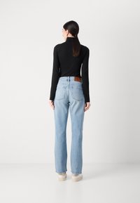 Lys blå denim jeans med en rett benpassform og en brun lær baklapp. Kombinert med en svart langermet topp, minimal design.