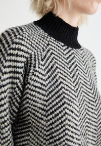 Maglione a maglia con colletto a coste nero, caratterizzato da un motivo a scacchi in nero e crema su tutto il corpo e una struttura a maglia testurizzata.