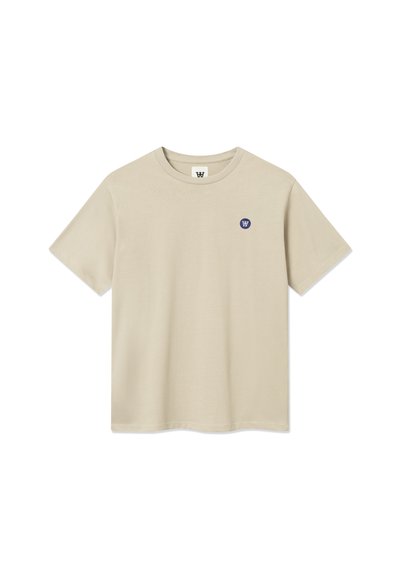 T-shirt en coton beige à manches courtes, col rond, avec un petit logo circulaire bleu sur la partie gauche de la poitrine. Texture lisse et coupe décontractée.