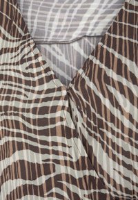 Braun und beige Stoff mit einem welligen Zebra-Streifenmuster, mit einem V-Ausschnitt-Design und weicher Textur, detaillierte Nähte am Ausschnitt.