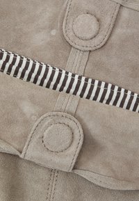 Beige mockasinsmaterial med en texturerad yta, tryckknappar och ett randigt foder i svart och vitt.