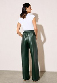 Zielone szerokie spodnie z ekologicznej skóry z elastycznym pasem, połączone z dopasowanym białym topem z krótkim rękawem. Gładka tekstura, minimalistyczny design.