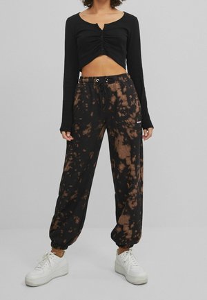 Czarny długi, krótki top z guzikami z przodu i prążkowaną fakturą, zestawiony z czarno-brązowymi joggerami w stylu tie-dye oraz białymi trampkami.