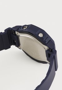 Orologio in gomma blu navy con fondello in acciaio inossidabile. Presenta una forma di cassa esagonale e due accenti a bottone sul lato. Finitura opaca.