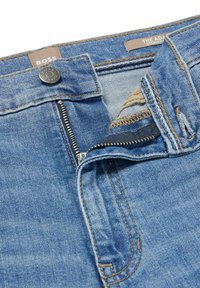 Modré džíny z denimu se rovnou siluetou, vybavené zipem, kovovým knoflíkem a hnědým prošíváním na pásu a kapsách.