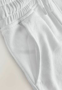 Pantalon en coton blanc avec une taille élastique, poches latérales et une finition douce et texturée. Détail en gros plan du tissu et des coutures.