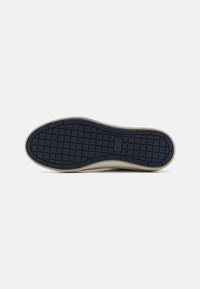Shoe sole with textured navy rubber, featuring a grid pattern for traction. Edge has a cream-colored border, highlighting a smooth transition.