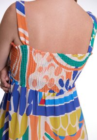 Multicolore jurk met een smok achterzijde, voorzien van levendige patronen in blauw, oranje, groen en geel, en brede schouderbanden.