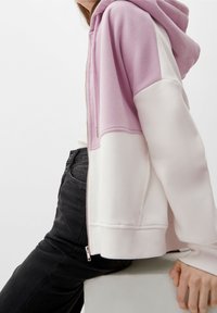 Felpa con cappuccio caratterizzata da blocchi di colore rosa e bianco, realizzata in tessuto morbido. Presenta una zip frontale e polsini e orlo a costine.