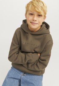 Sudadera verde oliva con un bolsillo frontal, que presenta un logo en texto oscuro. Combinada con vaqueros de mezclilla azul claro. Diseño simple y casual.