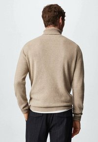 Pull en maille beige avec un col montant, des poignets et un ourlet côtelés. La texture semble douce, avec une finition lisse et sans motifs visibles.