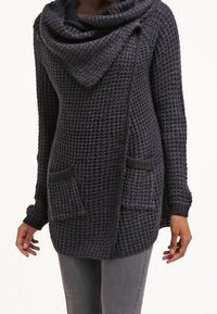 Texturerad mörkgrå stickad cardigan med stor krage, öppen framsida och två framfickor. Ärmarna är åtsittande och något avsmalnande.