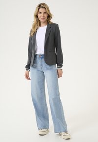 Grå blazer med kontrasterande randiga ärmar, över en vit t-shirt. I kombination med ljusblå vida jeans och vita sneakers.