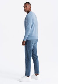 Sudadera azul claro con puños y dobladillo acanalados, combinada con jeans azul oscuro y zapatillas blancas. Enfocada en un diseño casual y cómodo.