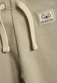 Beige ribbede bukser med snoreliv og et vævet mærke med et koala-design. Struktureret stof, blød finish og minimalistisk stil.