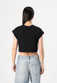 Juodas apkarpytas t-shirt su trumpomis rankovėmis, derinamas su aukštu juosmeniu šviesiai mėlynų džinsų, demonstruojantis paprastą dizainą ir minkštą tekstūrą.