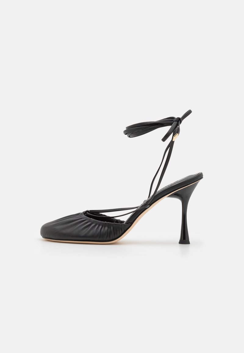 Fekete bőr hegyes orrú szandál, ráncolt részletekkel, bokakötővel és karcsú stiletto sarokkal. Simább textúra és minimalista design.