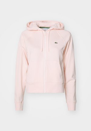 Sudadera con cremallera de color rosa claro en mezcla de algodón, con un bolsillo frontal, cremallera blanca y pequeño logo verde de Lacoste en el lado izquierdo del pecho.