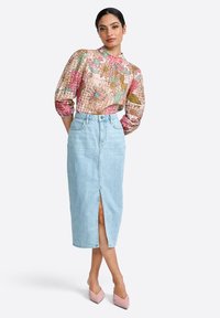 Blusa floreale con maniche a sbuffo, abbinata a una giacca di jeans blu chiaro con uno spacco frontale. Scarpe a punta rosa chiaro.