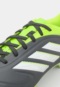 Schwarzer und neongrüner Fußballschuh mit strukturierter Oberfläche, ausgestattet mit drei weißen Streifen, Schnürsenkeln und einem glatten Fersendesign.