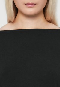 Crna majica bez ramena s glatkom teksturom i jednostavnim dizajnom, ističe ramena i području ključne kosti, bez vidljivih uzoraka ili akcenata.