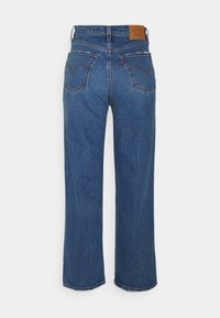 Jeans de mezclilla azul con un diseño de pierna recta, costuras visibles, dos bolsillos traseros y una etiqueta de cuero marrón en la cintura.