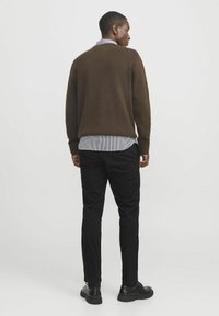 Brown knitted sweater over a light striped shirt, paired with black pants and black shoes, showcasing a relaxed fit and simple design.