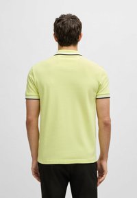 Limegrön polo skjorta i en slät tyg med en figursydd design, med en svart kant runt kragen och ärmsluten.