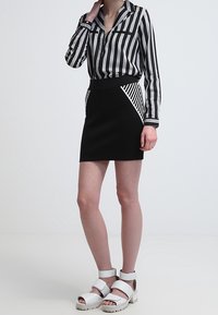 Mini gonna nera con motivo a strisce diagonali, abbinata a una blusa a maniche lunghe a strisce verticali bianco e nera. Sandali con plateau bianchi.