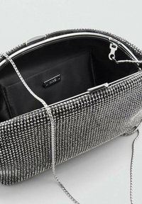 Pequeño bolso de mano negro cubierto de cuentas plateadas, con un cierre metálico y una correa de cadena, con un interior negro suave y una etiqueta de la marca.