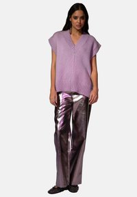 Un gilet en tricot violet clair avec un décolleté en V et une bordure côtelée, associé à un pantalon large en métal argenté brillant et des chaussures plates noires.