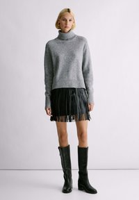 Maglione grigio a collo alto, con una vestibilità ampia, abbinato a una gonna in pelle nera con frange e stivali neri con tacco alti fino al ginocchio.