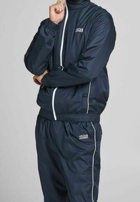 Chándal navy que incluye una chaqueta con cremallera y pantalones con cintura elástica, con detalles de piping blanco y un pequeño logo en el pecho y el muslo.