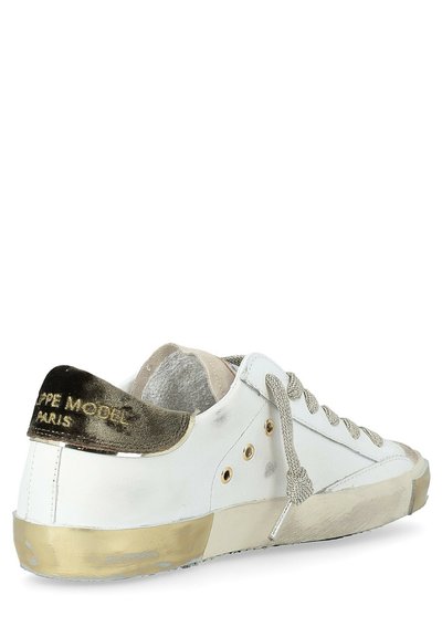 Baskets basses en cuir blanc avec une semelle beige usée, des lacets gris et un empiècement en métal doré au niveau du talon embossé avec "PEPE MODEL PARIS."