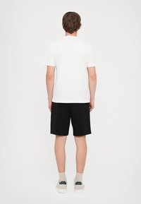 Hvit kortermet t-skjorte kombinert med svarte shorts, sett bakfra. Materialet ser mykt ut; ren design uten synlige mønstre eller aksenter.
