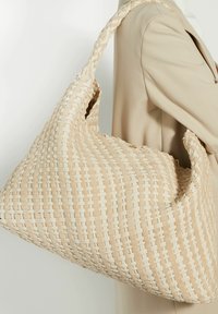 Geweven beige handtas met een slonzige vormgeving, met een gestructureerd oppervlak en een dikke, gevlochten schouderband. Toont een licht en donker geweven patroon.