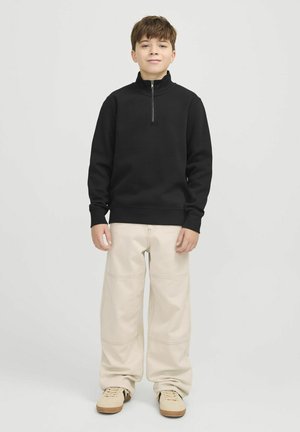Sweatshirt noir zippé avec un col montant, accompagné de pantalons beiges amples et de baskets beiges. Design simple et texture de tissu douce.