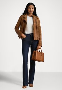 Hnedá kožená bunda s asymetrickým zipsom, biele tričko, tmavomodré rozšírené džínsy a malá hnedá kabelka. Hladké textúry a priliehavý strih.