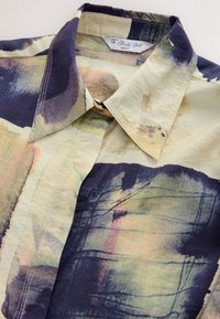 Collared button-up shirt featuring a cream base with abstract watercolor patterns in navy, green, and peach. Lightweight fabric with visible stitching.
