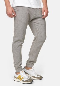Joggers gris clair évasés en tissu texturé, avec poches latérales et poignets élastiques, assortis à des chaussures de sport blanches et grises.