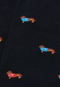 Tela navy con pequeños dachshunds bordados; algunos llevan suéteres azules y otros rojos con patrones de copos de nieve. Fondo de punto texturizado.