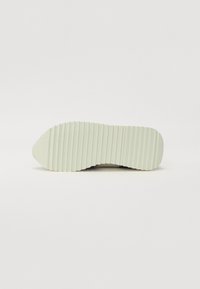 Semelle d'une chaussure avec une surface texturée et striée en vert clair, présentant un bout rond et un profil plat pour la stabilité.