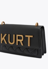 Sac à main en cuir noir avec un motif matelassé, des accents métalliques dorés et l'inscription audacieuse "KURT" sur le devant. Fermeture par rabat supérieur.