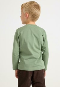 Langærmet, lysegrøn bomulds T-shirt med rund halsudskæring, glat tekstur og afsluttet kant. Sammen med brune fløjl bukser.