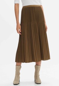 Jupe midi plissée marron en tissu léger, dotée d'une taille lisse et d'une texture fluide, associée à des bottes à talons beiges.