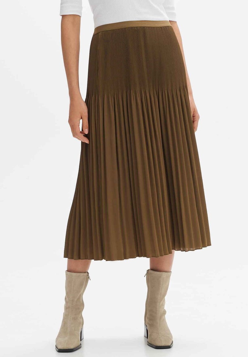 Jupe midi plissée marron en tissu léger, dotée d'une taille lisse et d'une texture fluide, associée à des bottes à talons beiges.
